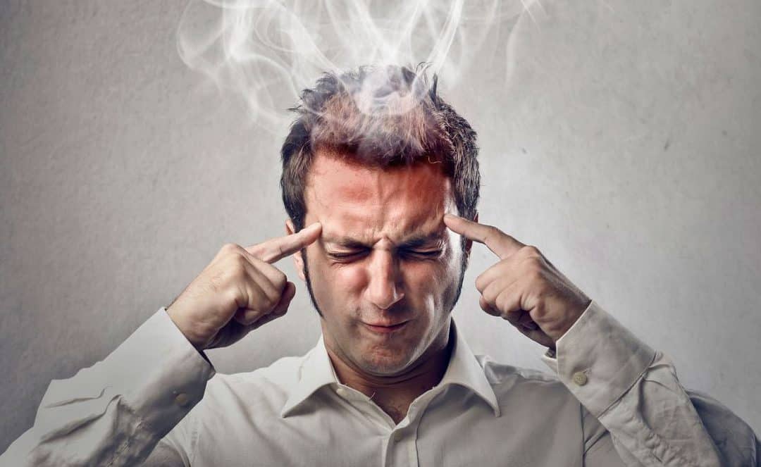 Man with brain fatigue looking down with steam coming off his head and fingers pointing to his head